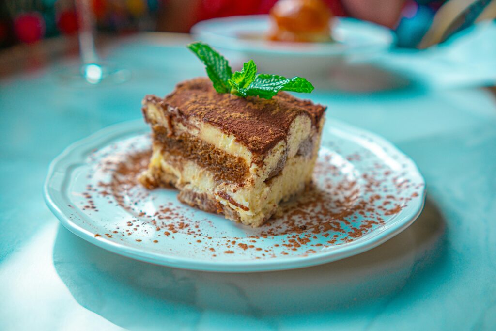 Mouth-watering slice of tiramisu with mint garnish on a white plate, perfect for dessert lovers and fans of classic Italian foods.