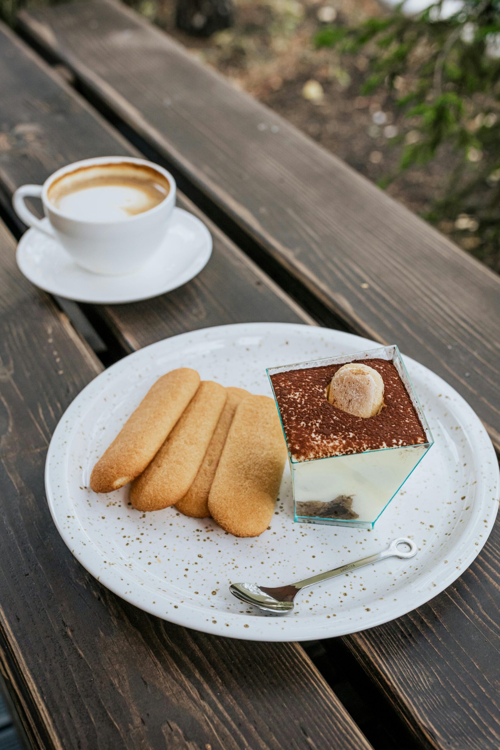 Tiramisu dessert with ladyfingers and coffee on a rustic wooden table outdoors at an Italian Restaurant. Let me know if you'd like alternate versions or more descriptive wording