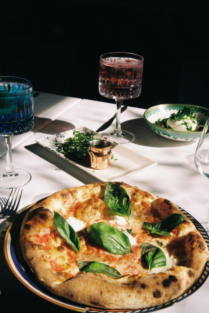 Fresh Italian pizza with basil on a table with drinks and side dishes.