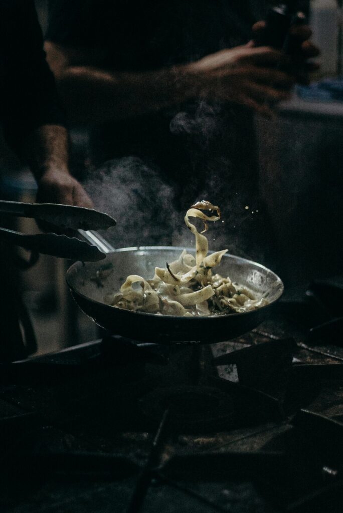 Chef skillfully tosses pasta in a steaming pan, showcasing culinary expertise.