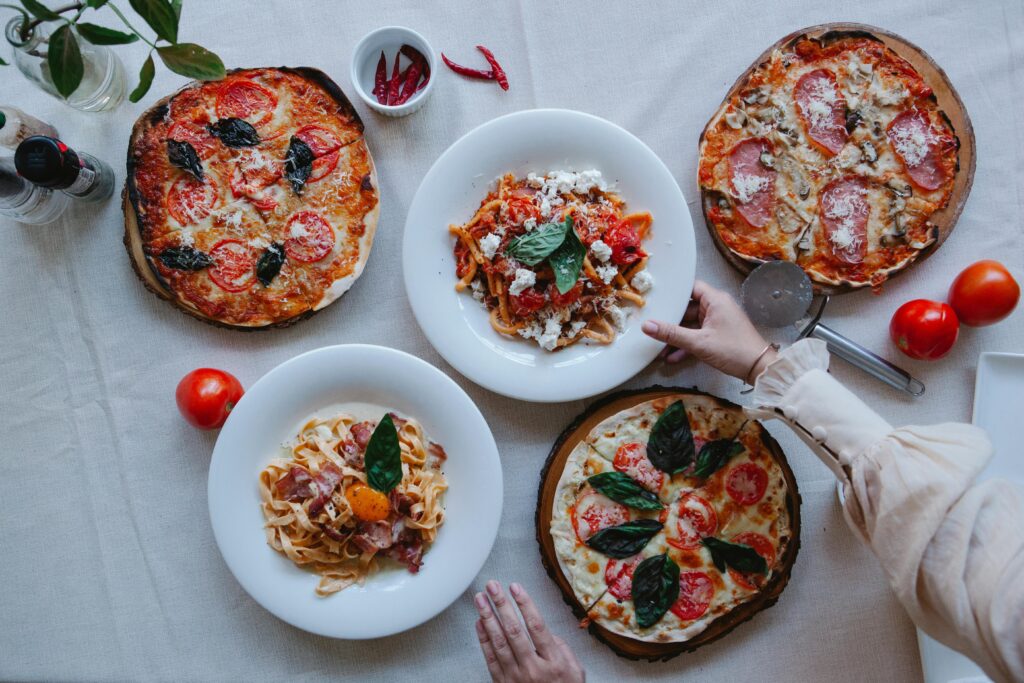 Top view of pizzas and pastas beautifully arranged on a table, ideal for food photography.