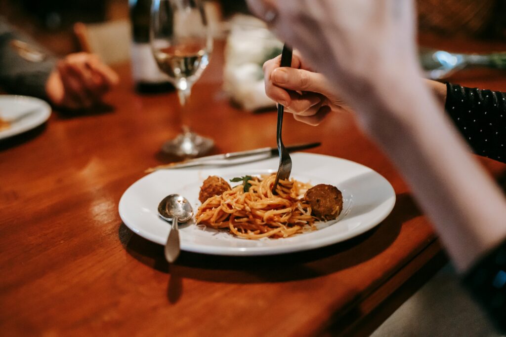 Crop anonymous female enjoying tasty yummy spaghetti with meat ball and glass of white wine in restaurant